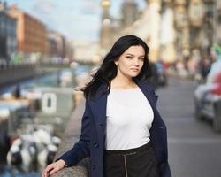 Portrait f beautiful intelligent brunette who walks down street of Saint-Petersburg in city center. Charming thoughtful woman with long dark hair wanders alone, immersed in thoughts photo