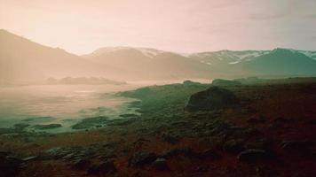 Clear river with rocks leads towards mountains lit by sunset video