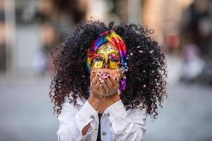 Carnaval party. Brazilian curly hair woman in costume blowing confetti photo