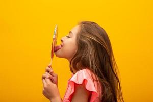 The child is holding a lollipop. Childish joy is sweetness. Little girl on yellow background. photo