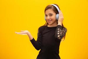A little cute girl enjoying listening music by headphone introducing brand or product on the side isolated on yellow background. photo
