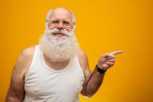 Old man with a long beard pointing side on a yellow background. Senior with full white beard. Old man with a long beard with sadness. photo