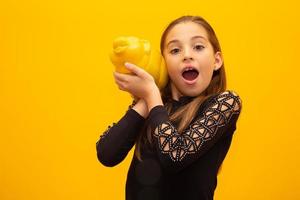 niña caucásica sobre fondo amarillo aislado sosteniendo una gran alcancía. foto