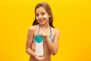 Child holding a bottle of sunscreen on white. Introducing a product. Concept of summer, beach and pool. photo