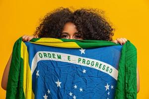 Misterious black woman fan holding a Brazilian flag in your face. Brazil colors in background, green, blue and yellow. Elections, soccer or politics. photo