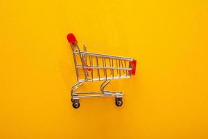Empty shopping cart over yellow background, mini metal cart on color background