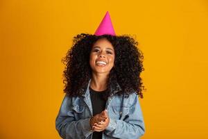 joven afroamericana con sombrero de cumpleaños sobre un fondo amarillo aislado con una sonrisa alegre y fresca en la cara. persona con suerte. foto