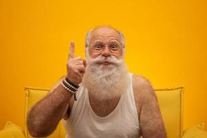 senior sonriente con un hombre de larga barba blanca haciendo un gesto de señas con los dedos de la mano sobre fondo amarillo. emoción positiva expresión facial sentimientos, actitud, símbolo, cuenta regresiva. foto