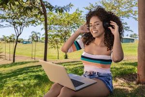 Beautiful afro american girl listening music on laptop in a park photo