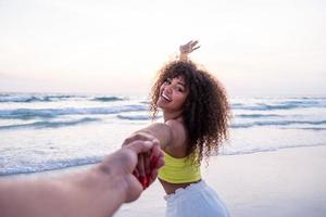 Girl holding male hand and running on tropical exotic beach to the ocean. Follow me shot of young woman pull her boyfriend on the sea shore. Summer vacation or holiday. POV.
