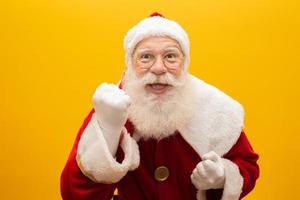 Holly jolly x-mas and Noel, confidence, magic, triumph concept. Cool funny playful grandfather with wide open mouth, comic grimace, fooling around isolated on yellow background, shows win gesture photo