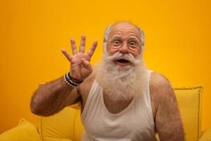 senior sonriente con un hombre de barba blanca larga haciendo cuatro veces el gesto de señas con los dedos de la mano sobre fondo amarillo. emoción positiva expresión facial sentimientos, actitud, símbolo, cuenta regresiva. foto