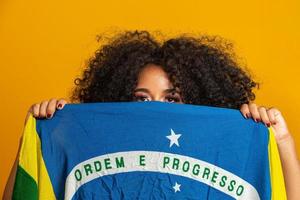 Misterious black woman fan holding a Brazilian flag in your face. Brazil colors in background, green, blue and yellow. Elections, soccer or politics. photo