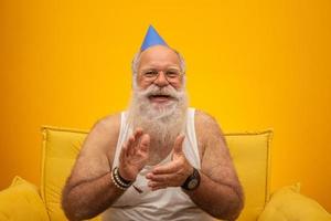 Positive elderly man in party hat smiling to camera, birthday celebration photo
