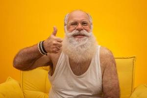 Old man with a long beard on a yellow background. Thumb up. Senior with full white beard. Old man with a long beard with sadness. photo