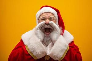 Communication concept. Profile side view photo of excited funny kind stylish Santa Claus with open mouth hold palm hand near face saying loud ho-ho-ho isolated on vivid yellow background