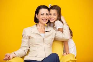 Happy mother's day Close up portrait of pretty, charming mother and daughter with beaming smiles over yellow background. Daughter hugging mother on yellow background. photo