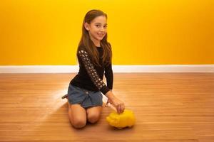 Caucasian little girl over yellow background holding a big piggybank. photo