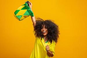 partidario de brasil. fan brasileña celebrando el fútbol o el partido de fútbol con fondo amarillo. colores de brasil. foto