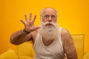 senior sonriente con un hombre de barba blanca larga haciendo cinco veces el gesto de señas con los dedos de la mano sobre fondo amarillo. emoción positiva expresión facial sentimientos, actitud, símbolo, cuenta regresiva. foto