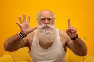 senior sonriente con un hombre de barba blanca larga haciendo seis veces el gesto de señas con los dedos de la mano sobre fondo amarillo. emoción positiva expresión facial sentimientos, actitud, símbolo, cuenta regresiva. foto