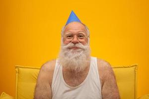 Positive elderly man in party hat smiling to camera, birthday celebration photo