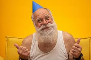 anciano positivo con sombrero de fiesta sonriendo a la cámara, celebración de cumpleaños foto