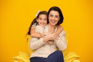 Happy mother's day Close up portrait of pretty, charming mother and daughter with beaming smiles over yellow background. Daughter hugging mother on yellow background. photo