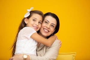 feliz día de la madre primer plano retrato de madre e hija bonitas y encantadoras con sonrisas radiantes sobre fondo amarillo. hija abrazando a la madre sobre fondo amarillo. foto