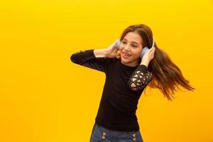 una niña linda que disfruta escuchando música con auriculares aislados en un fondo amarillo. foto