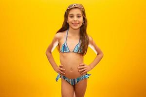 Child wearing bikini on yellow background. Concept of summer, beach and pool. photo
