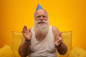 anciano positivo con sombrero de fiesta sonriendo a la cámara, celebración de cumpleaños foto