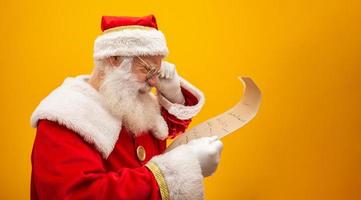 Happy Santa Claus holding vintage paper on yellow background. Merry Christmas and New Year's Eve concept. Copy space. Difficulty reading. Ugly handwriting.