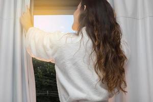 people and hope concept - close up of happy woman opening window curtains photo