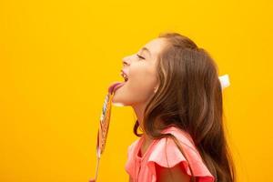 The child is holding a lollipop. Childish joy is sweetness. Little girl on yellow background. photo