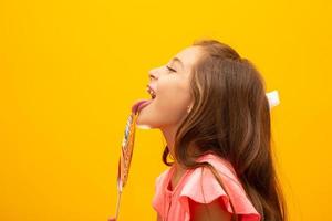 The child is holding a lollipop. Childish joy is sweetness. Little girl on yellow background. photo