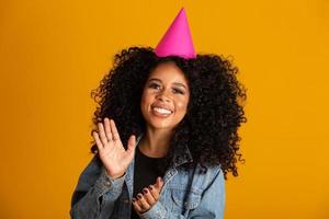 Young afro american woman wearing birthday hat over isolated yellow background with a happy and cool smile on face. Lucky person. photo