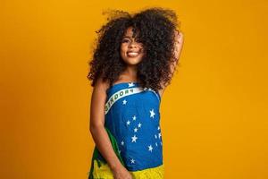 Happy black woman fan holding a Brazilian flag. Brazil colors in background, green, blue and yellow. Elections, soccer or politics. photo