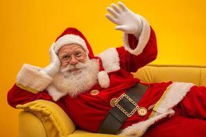 Santa Claus sitting on a yellow couch on yellow background with copy space. Yellow sofa. photo