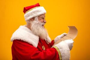 Happy Santa Claus holding vintage paper on yellow background. Merry Christmas and New Year's Eve concept. Copy space. Difficulty reading. Ugly handwriting. photo