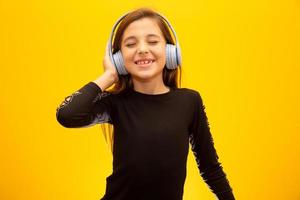 A little cute girl enjoying listening music by headphone isolated on yellow background. photo