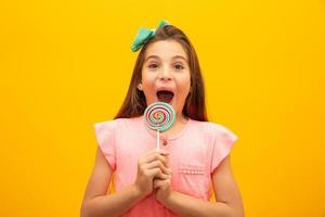 The child is holding a lollipop. Childish joy is sweetness. Little girl on yellow background.