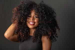 joven mujer afroamericana con cabello rizado mirando a la cámara y sonriendo. linda chica afro con cabello rizado sonriendo mirando a la cámara. foto