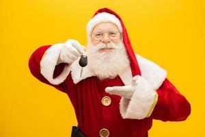 Santa Claus holding keys of a car on yellow background. photo