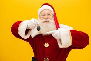 Santa Claus holding keys of a car on yellow background. photo