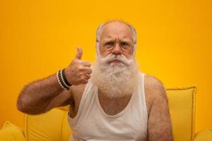 Old man with a long beard on a yellow background. Thumb up. Senior with full white beard. Old man with a long beard with sadness. photo