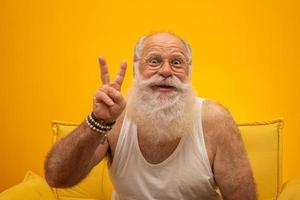 senior sonriente con un hombre de barba blanca larga haciendo dos veces el gesto de señas con los dedos de la mano sobre fondo amarillo. emoción positiva expresión facial sentimientos, actitud, símbolo, cuenta regresiva. foto