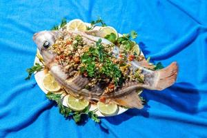 Close-up above, a large whole fish steamed in lime in a dish that is placed on a blue cloth. photo