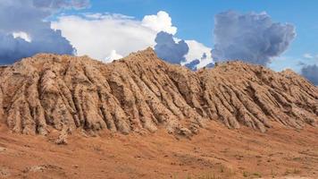 A large mound of sandy soil eroded by rainwater and sky clouds. photo