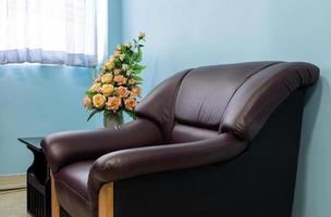 Brown sofa armchair with a bouquet of roses in a blue wall. photo